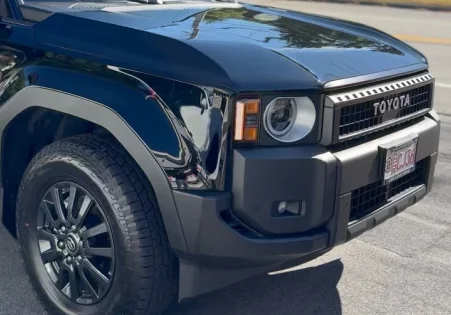 Close-up of a black Toyota SUV with glossy window tint and custom black wheels parked on a sunny street.