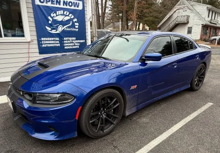 Blue Dodge Charger with dark-tinted windows parked in front of a tinting service shop displaying signage for automotive and residential tinting.
