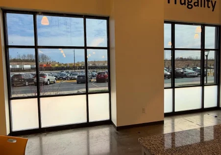 Large commercial windows with the bottom panes tinted white for privacy while upper panes remain clear, showing a parking lot outside.