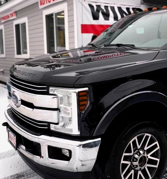 Front side view of a black Ford Super Duty truck with tinted windows, parked outside a tinting shop.