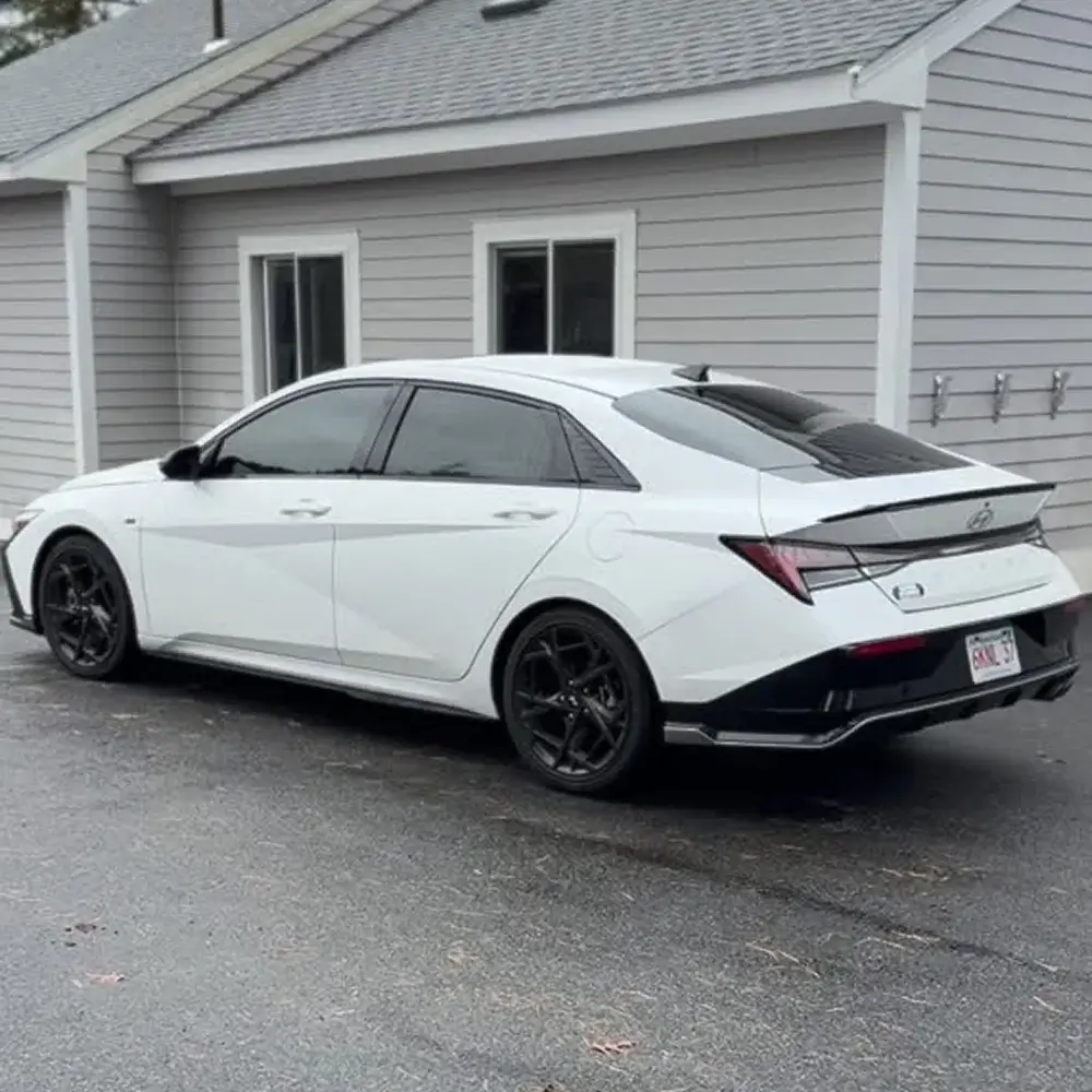 White Hyundai Elantra with dark-tinted windows and black wheels parked outside a residential-style building.