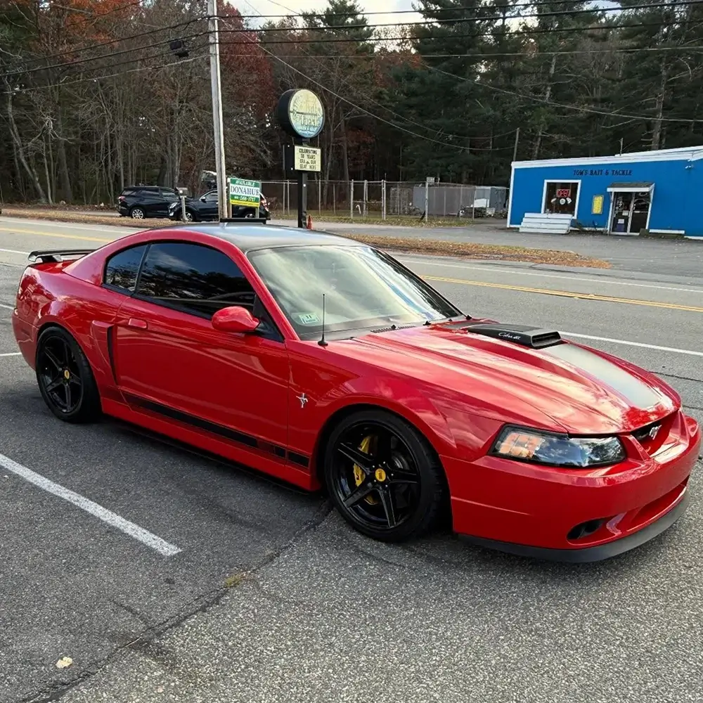 Red Ford Mustang coupe with black accents and dark tinted windows parked in a roadside lot.