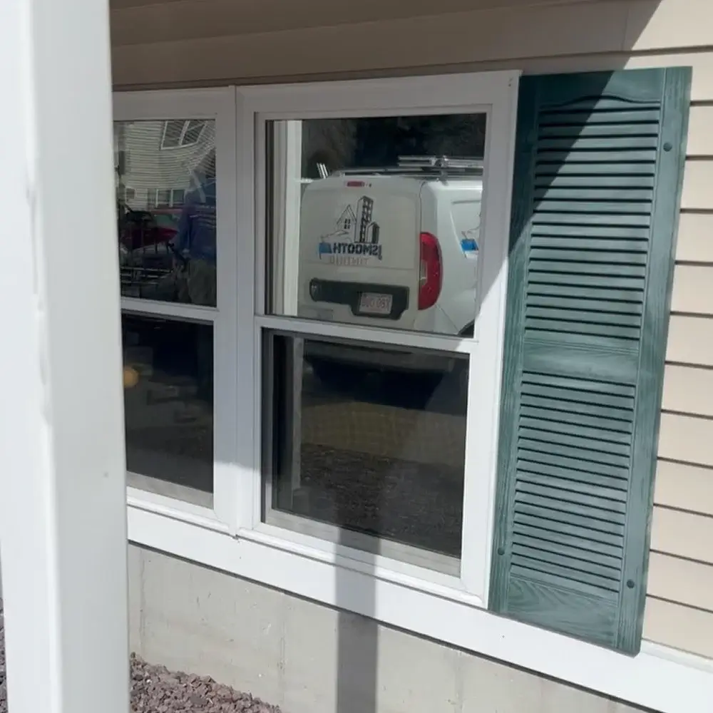 White-framed residential window with subtle tint and blue shutters, reflecting a JSmooth Tinting van.