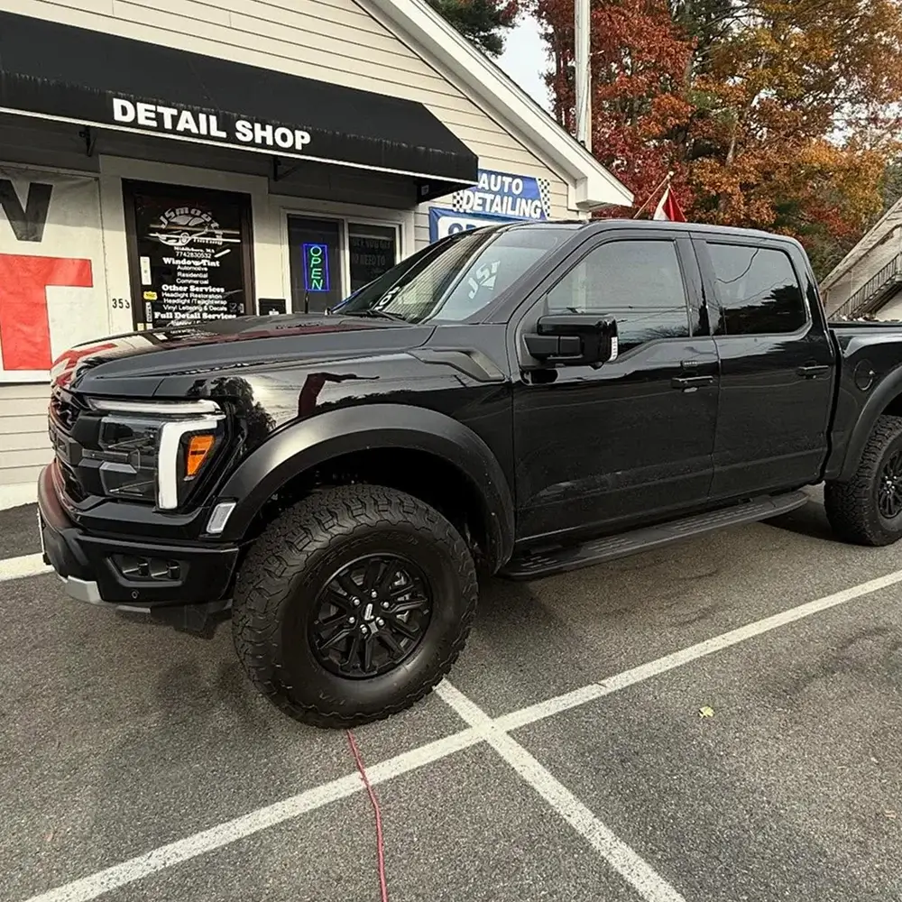 Black Ford pickup truck with dark window tint parked in front of an auto detailing shop.