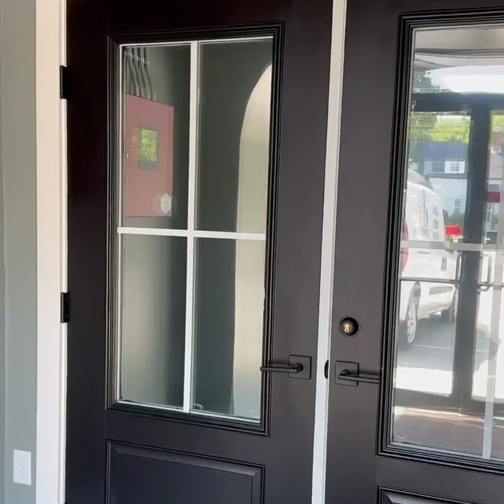 Black double front door with clear divided glass panels, one side showing a semi-reflective privacy tint.
