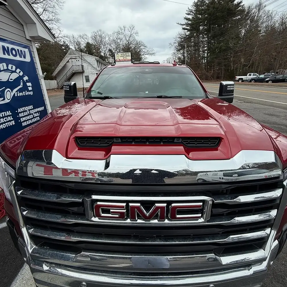 Front view of a red GMC truck with chrome accents and darkly tinted windows parked in front of a tinting shop.