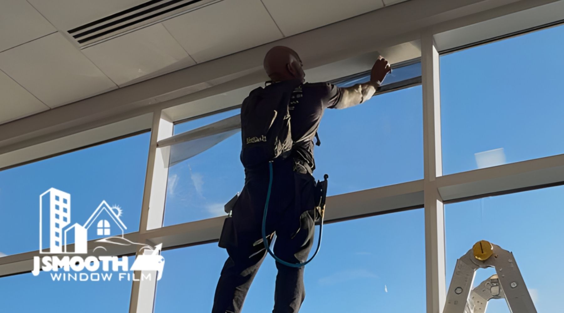 A professional window tinter stands on a ladder while applying film to a tall residential window, with a clear blue sky in the background. Text overlay reads “What is Residential Window Tinting in Middleborough, MA?” alongside the J Smooth Window Film logo.