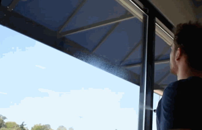 A man sprays cleaning solution onto a large commercial window in preparation for window tint film application as part of a commercial window tinting project.