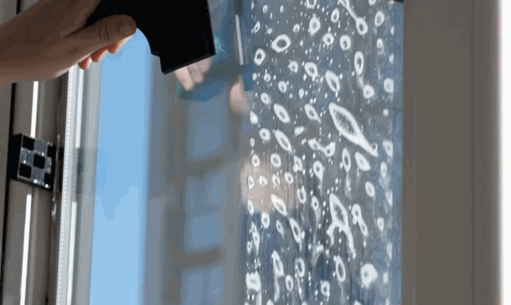 Close up of a hand using a squeegee to remove bubbles from commercial window tint on a glass pane covered in soapy solution. The film is gradually becoming clear as it adheres to the surface.