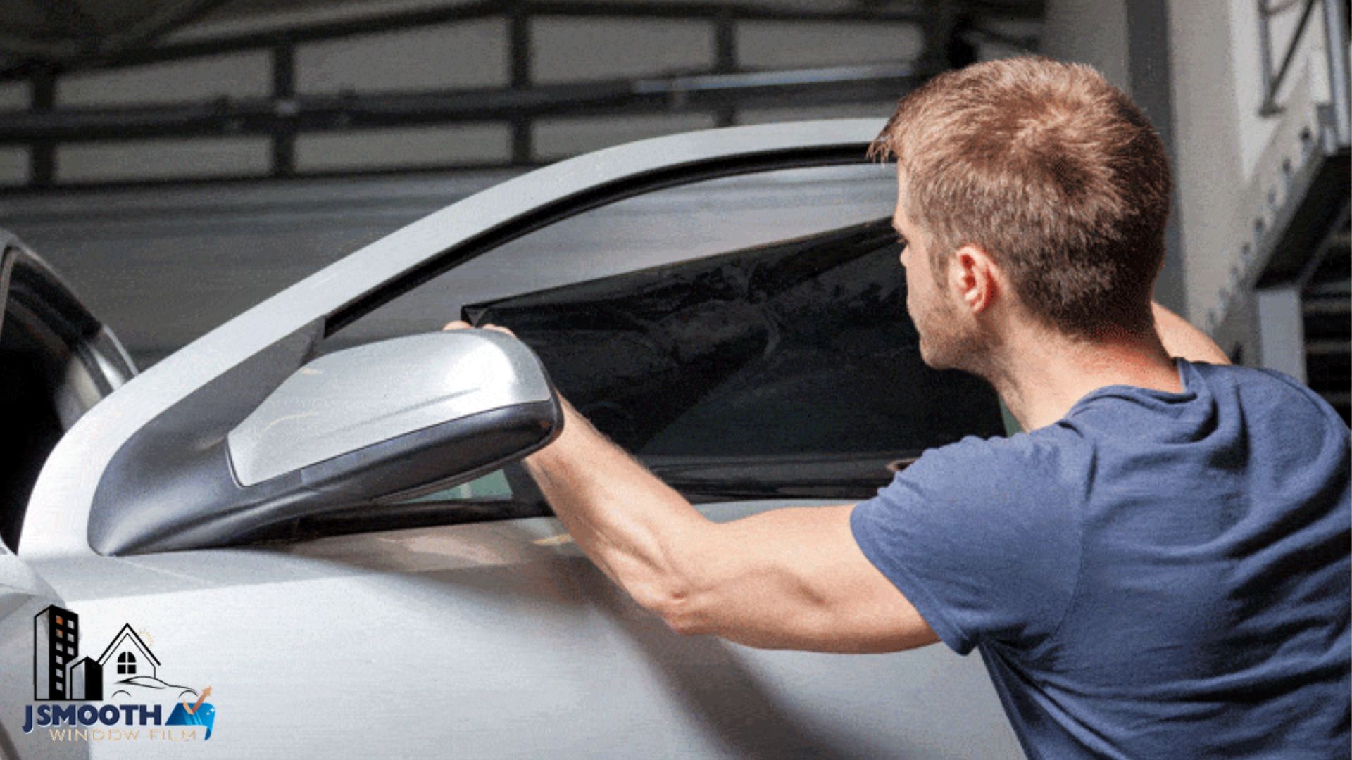 A technician applies ceramic window tint to the side window of a white car in a garage. The car door has a logo that reads "JSMOOTH WINDOW FILM".