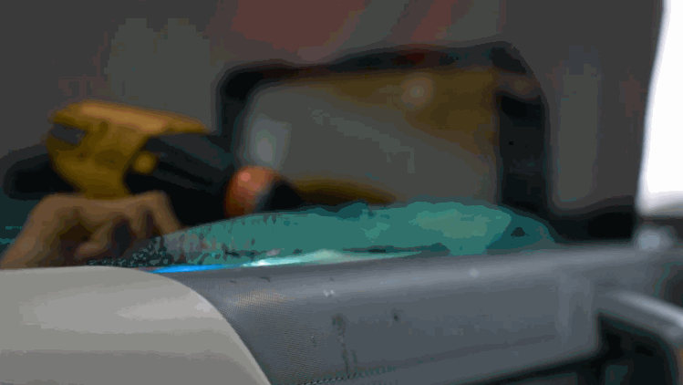 A technician uses a yellow heat gun to shape ceramic window tint along the top edge of a vehicle window. The film is being formed for a smooth precise fit.